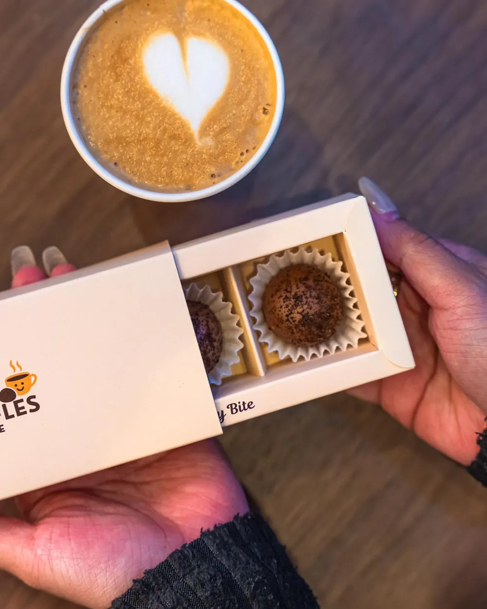 Someone opening a Happy Truffles box next to a latte